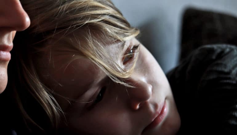 child leans on mother's shoulder in dim light