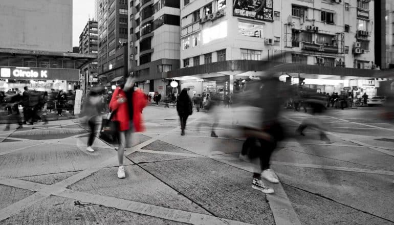 red coat on pedestrian in b/w image of busy crosswalk