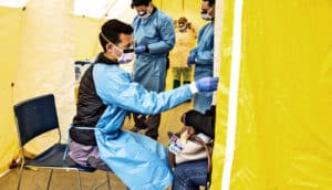 A health care worker tests a patient for COVID-19 inside a yellow tent