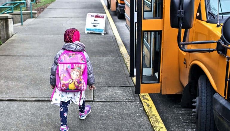 A young girl walks to a school bus after her school closes