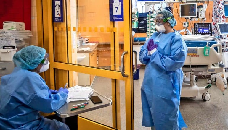 medical worker at door of hospital room and another seated at desk with paperwork