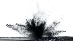 Black dirt and debris bursts from the ground after an impact, with a white background