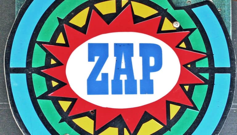 A shooting range target has blue, green, and yellow concentric circles with a red starburst with the word "ZAP" in it