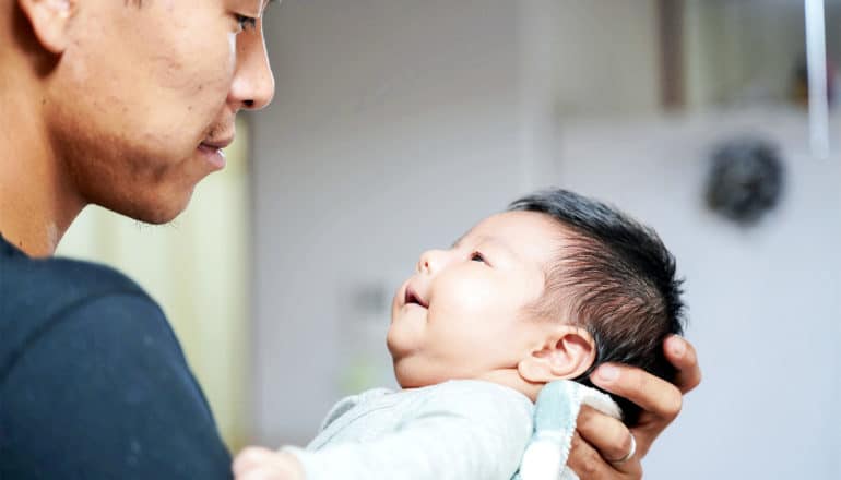 A baby looks up at a man's face while smiling