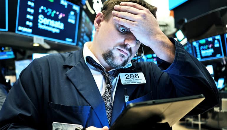 A stock trader puts his hand to his forehead in worry