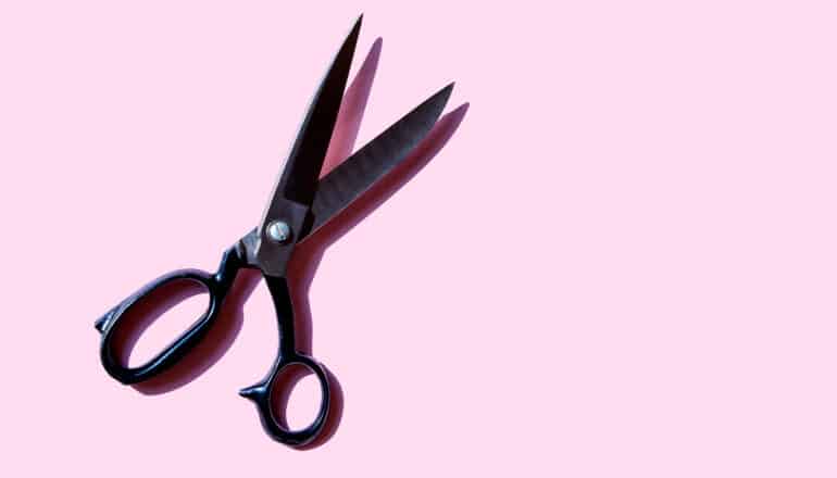 A pair of black-handled scissors sit on a pink background