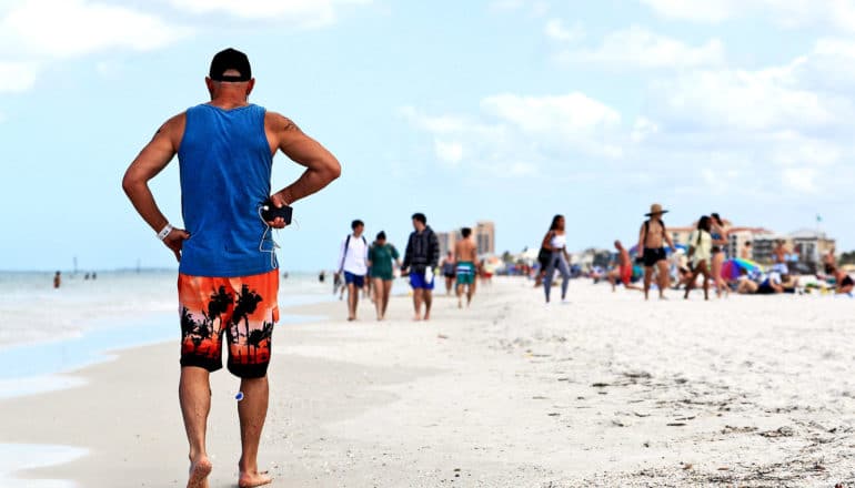 A man walks down a crowded Florida beach, packed with spring breakers