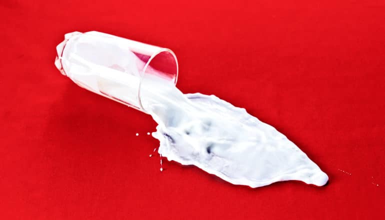 A glass of milk spills on a red surface