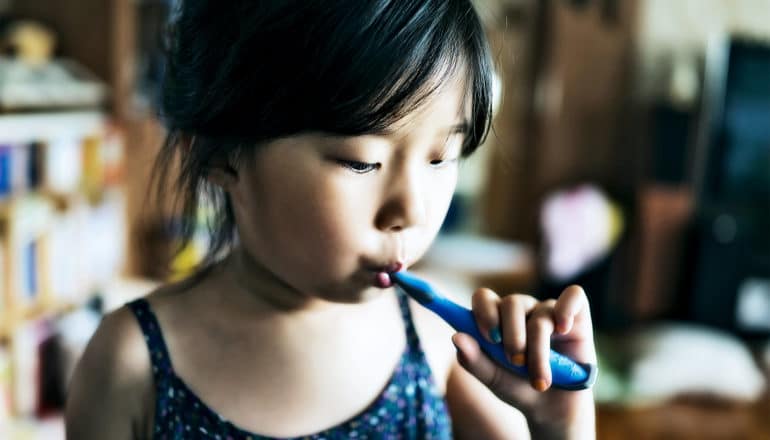 A young girl looks down at her toothbrush while brushing her teeth