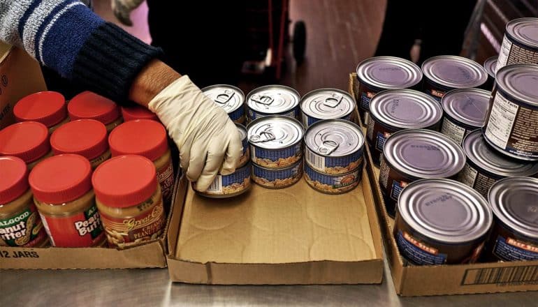 A person wearing gloves stocks a food pantry with cans of tuna