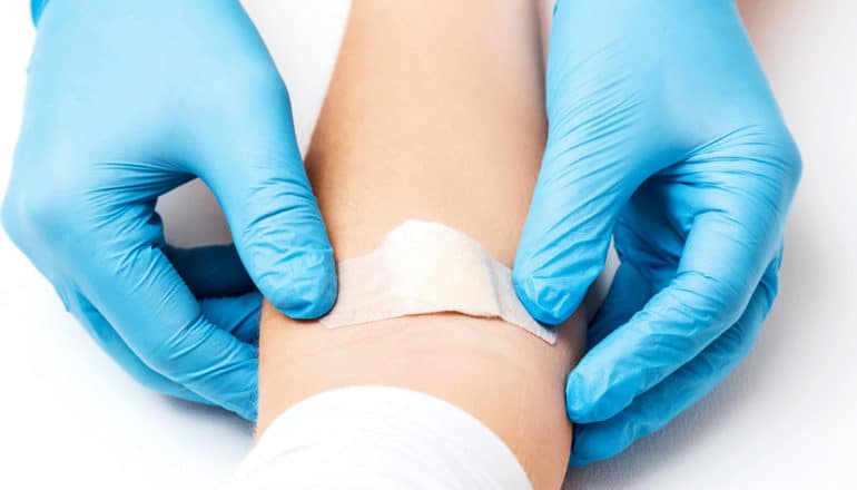 A doctor with blue gloves puts a bandage and cotton ball over a blood draw on a person's arm