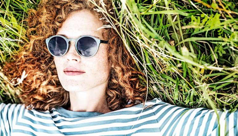 A woman in a striped t-shirt and sunglasses lays in long grass