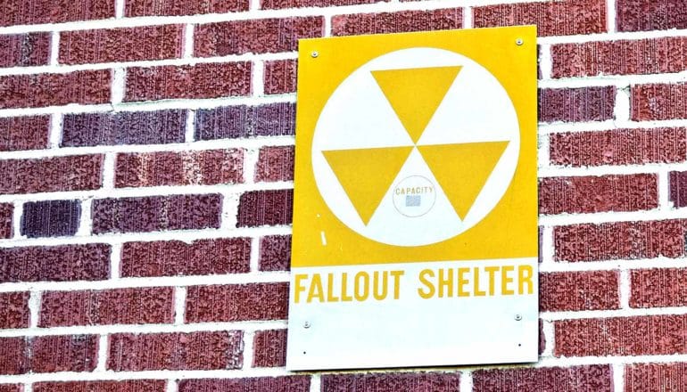 A fallout shelter sign is bolted to a brick wall