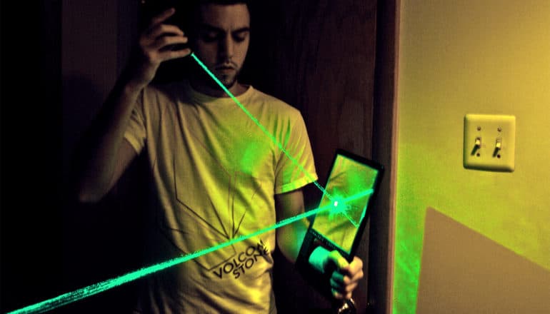 A man aims a green laser at a mirror