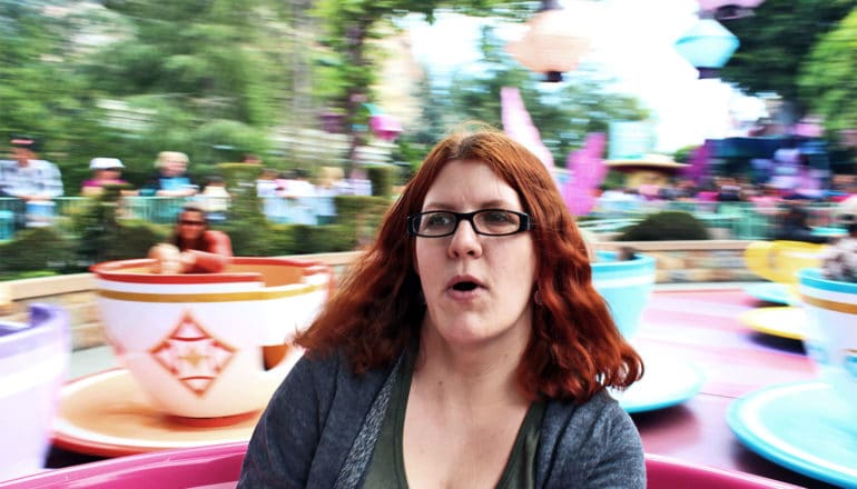 A woman rides the Disneyland teacups ride while making an overwhelmed expression, the background a blur behind her