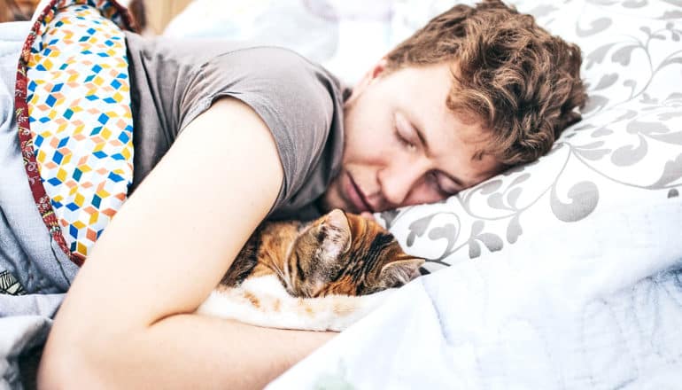 A woman sleeps in bed with her cat close by under the covers