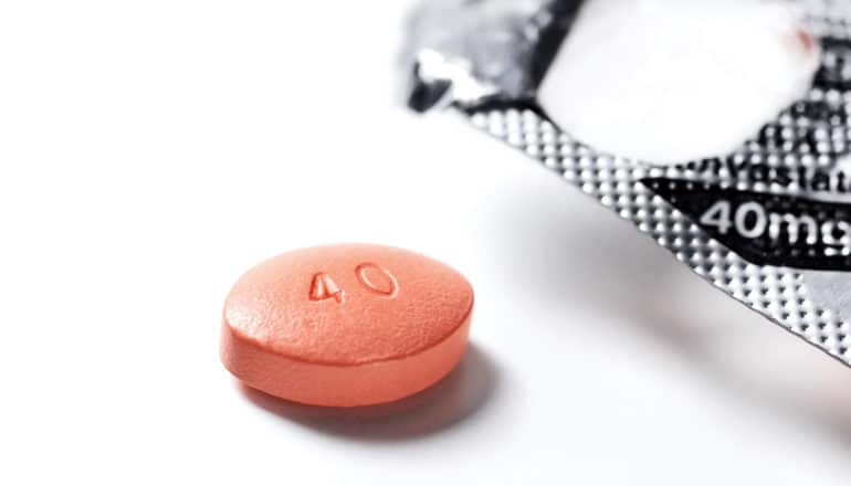 An reddish-orange pill with "40" stamped on it sits on a white background near an opened pill packet