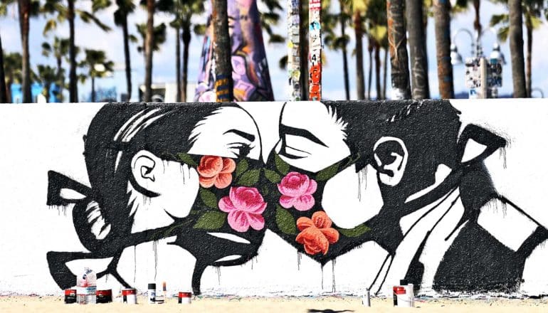 A mural on a white wall shows two people kissing while wearing medical masks