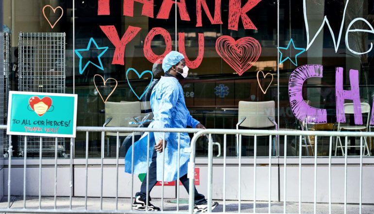 A doctor in blue protective gear and a white face mask walks past