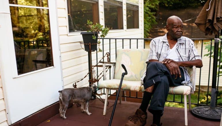 older man on sits on porch with dog and cane