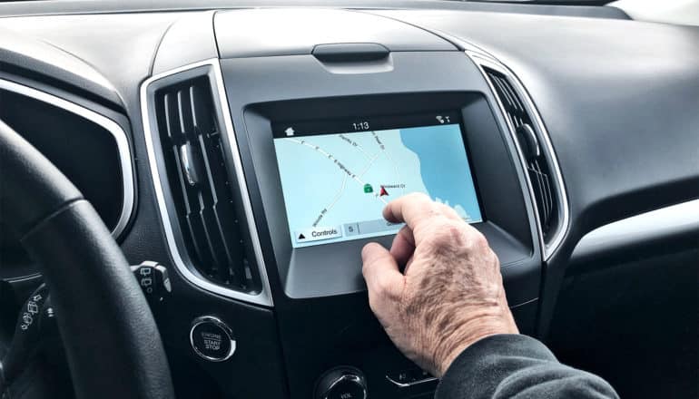 An older man reaches his hand out to touch the GPS screen in a car