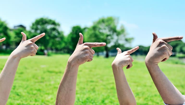 Four hands point to the right with grass and sky in the backgroun