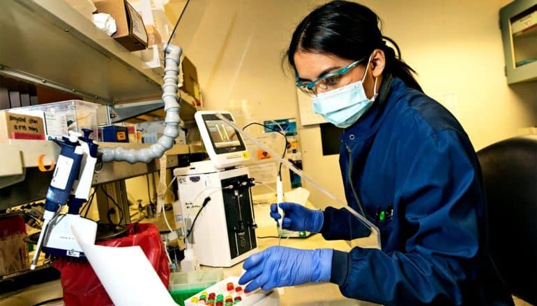 A researcher wears a mask and gloves as she works in the lab