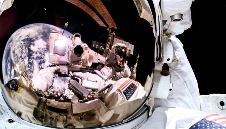 A reflection in an astronaut's helmet shows Earth and the camera he's using to take the photo