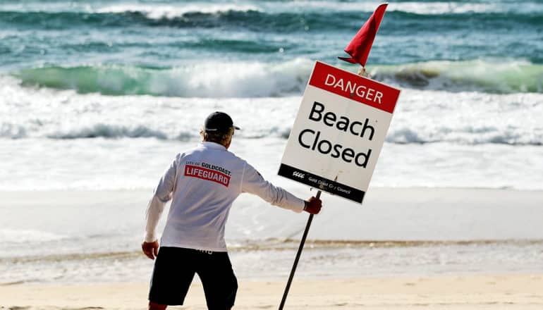 A lifeguard places a sign on the beach that says "Beach Closed"