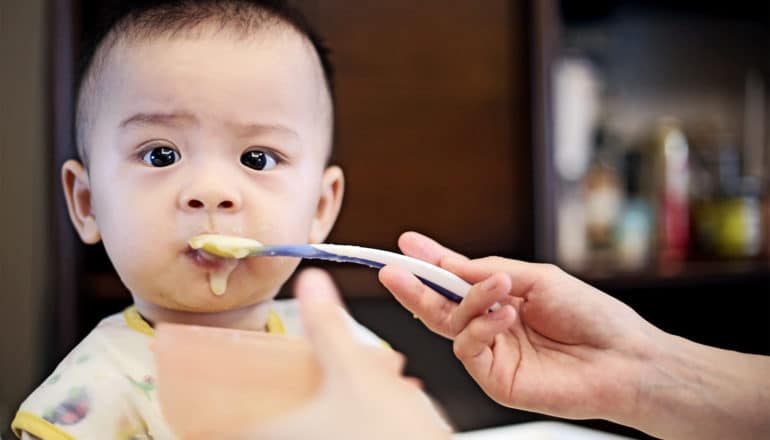 A parent feeds a baby food that's dribbling down his face