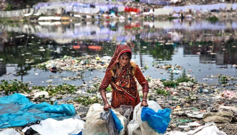 A woman washes plastic in a river filled with trash