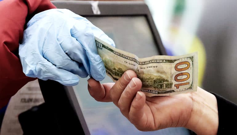 A gloved customer hands a 100 dollar bill to a worker at a grocery store cash register