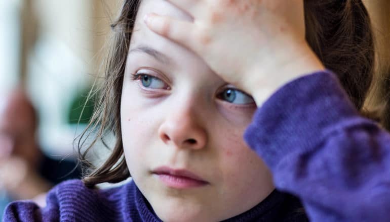 worried-looking child looks aside with hand on forehead