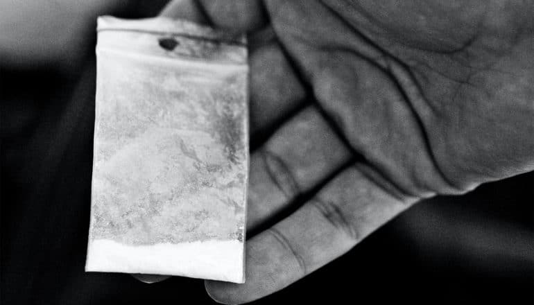 A person holds a small bag of cocaine