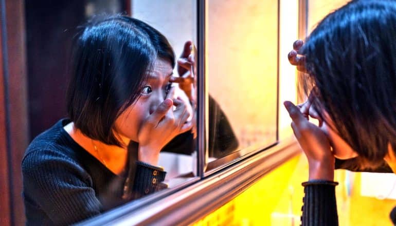 A young woman puts in her contact lenses in front of the mirror