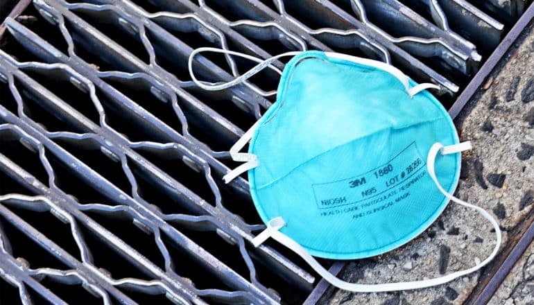 A blue medical mask sits on a sewer or subway grate