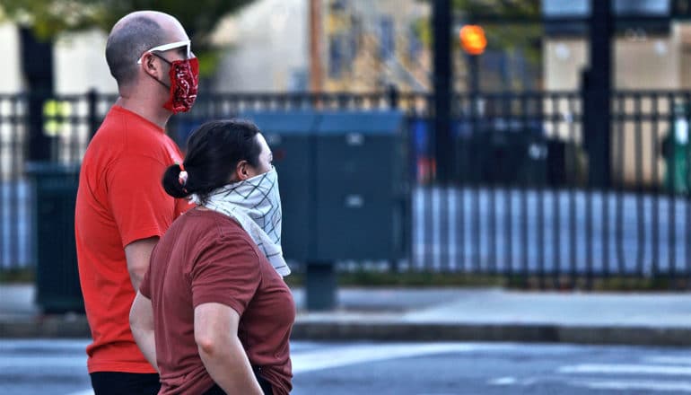 Two people wearing homemade masks walk down the street together