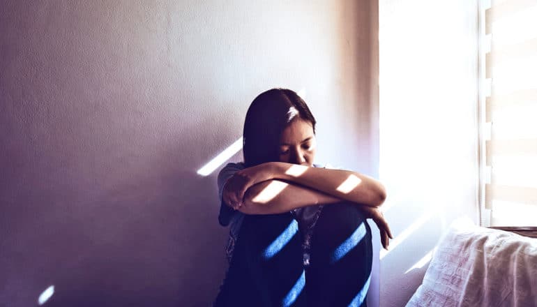 A young woman sits by the window leaning on her knees