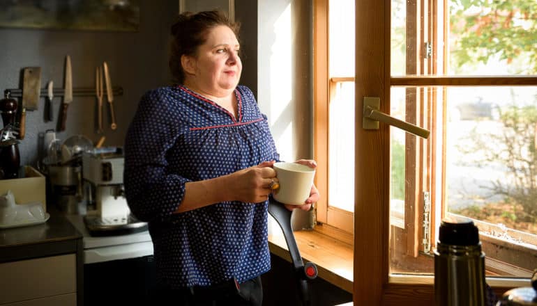 person with crutches holds mug and looks out window