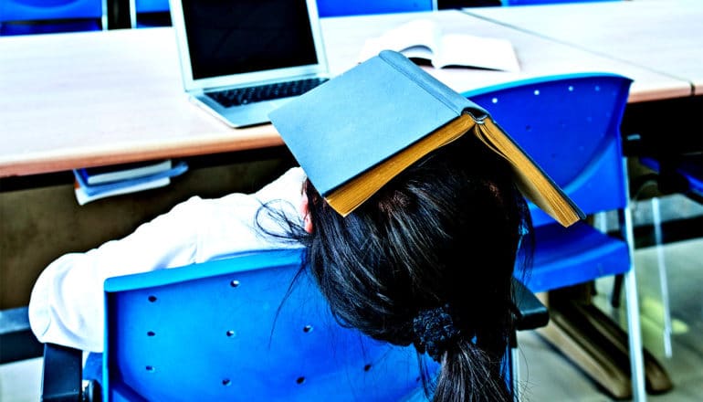 A young woman sleeps with a book over her face in a school library