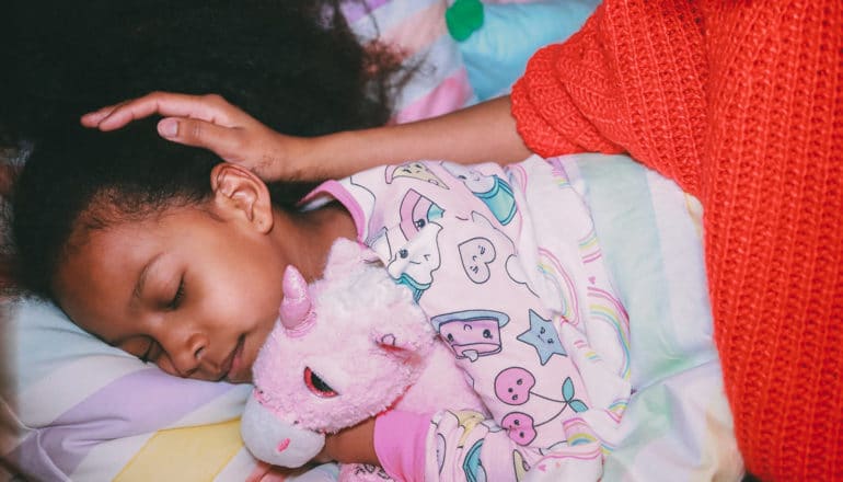 adult pats head of sleeping child clutching stuffed unicorn