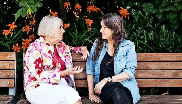 A mother speaks with her daughter on a park bench