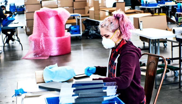 A pink-haired manufacturing worker makes face masks in a large warehouse