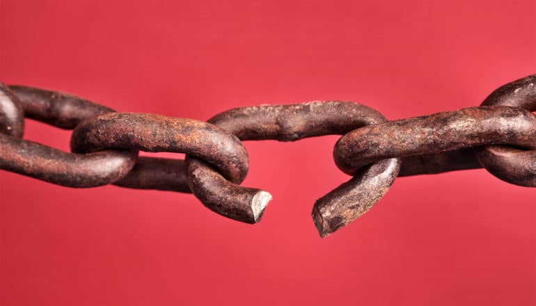 A link in a rusty chain breaks against a red background