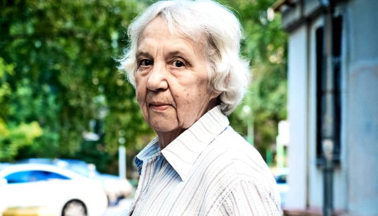 An older woman in a white collared shirt looks at the camera