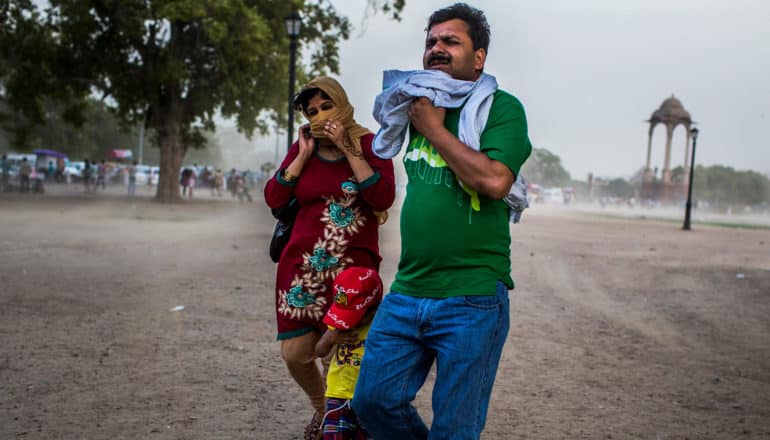 two adults and child cover their faces on dusty street