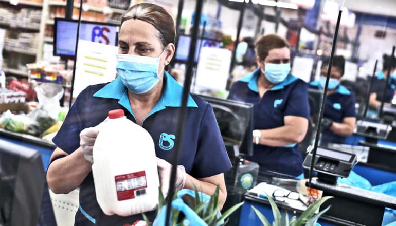 Grocery store workers wear masks and gloves as they bag groceries and check customers out