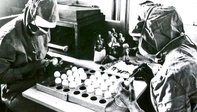 Two people in protective gear work with eggs on a measles vaccine