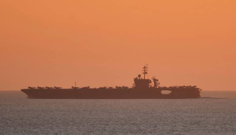 aircraft carrier in silhouette against orange sky