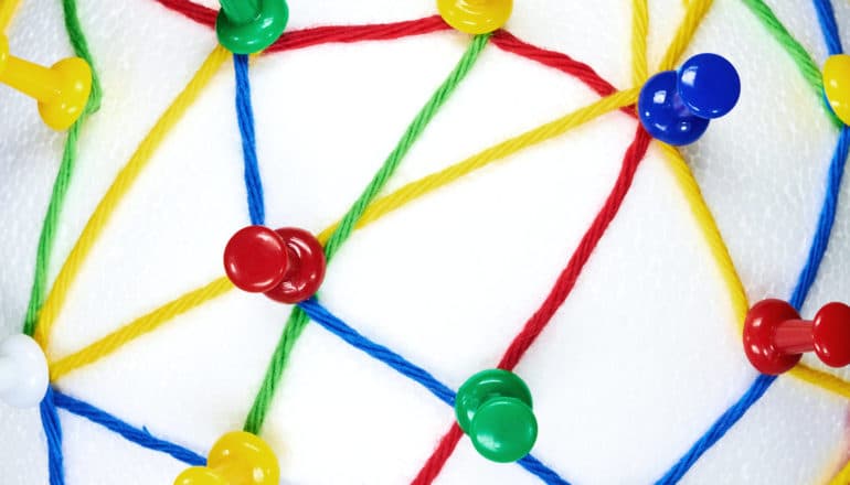 A series of colorful thumbtacks hold a web of colored string